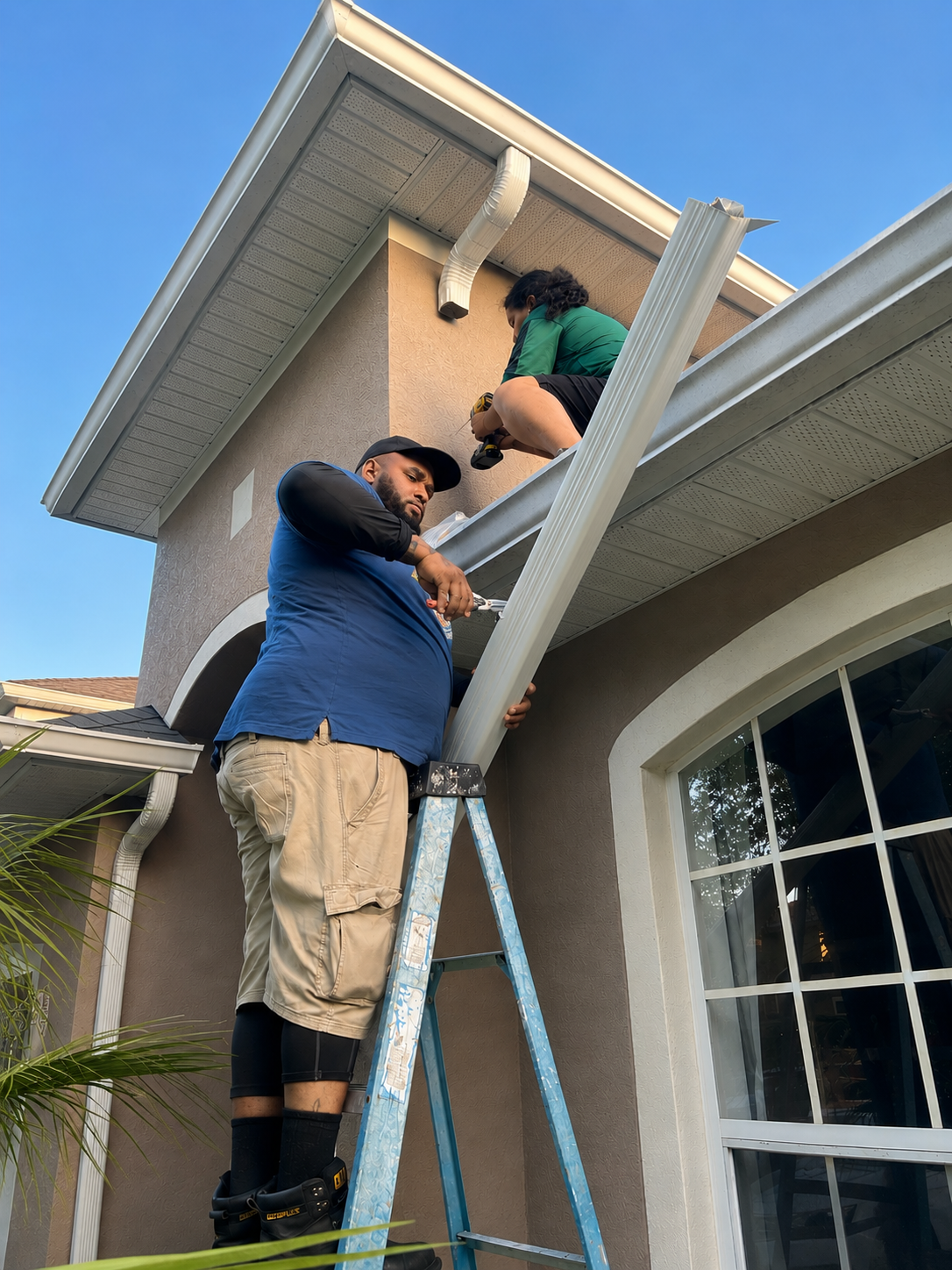 Two installers working on finishing a downspout Professional gutter installers working on a seamless gutter and downspout installation in Orlando Florida